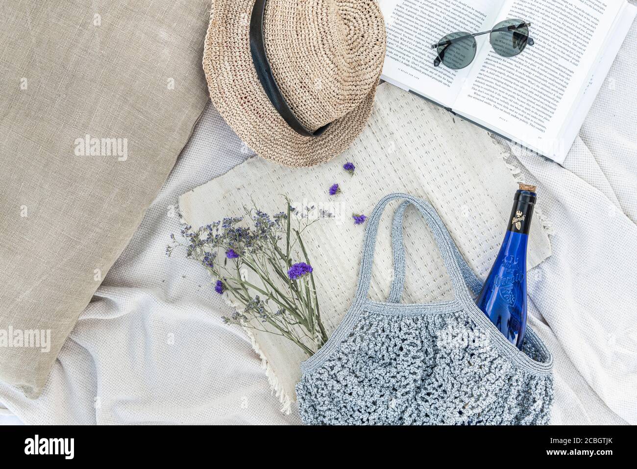 Bottiglia di vino, lavanda viola e un libro su una coperta da picnic in spiaggia in una calda giornata estiva Foto Stock