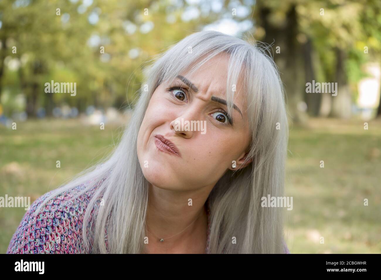 Ritratto all'aperto di una donna che fa volti divertenti. Capelli d'argento. Foto Stock