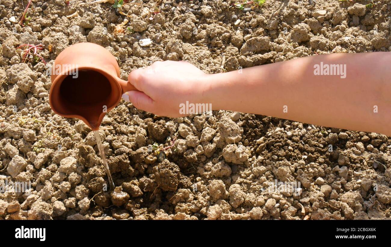 Versare acqua con una pentola su terreno asciutto nel fattoria Foto Stock