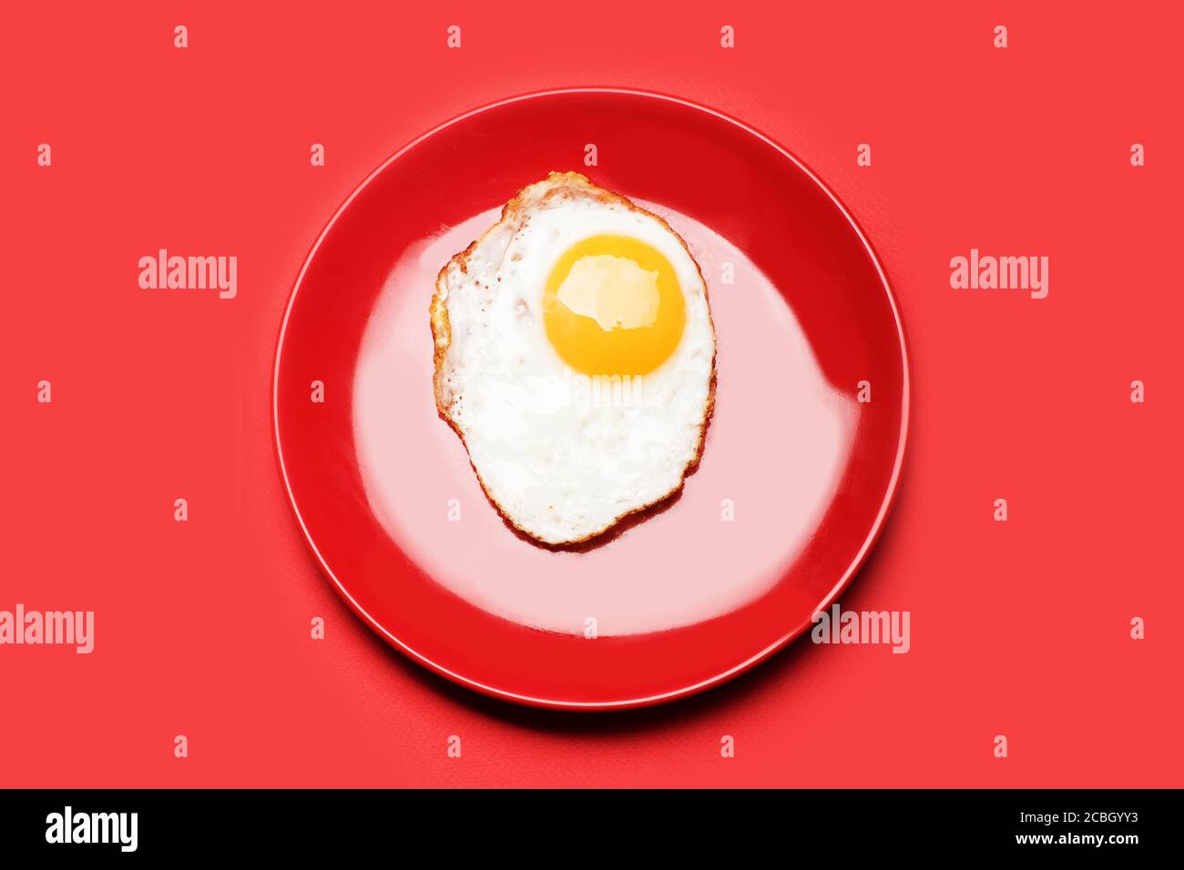 Piatto con uovo fritto e tuorlo crudo. Cibo posto su piastra rossa su sfondo rosso, vista dall'alto. Colazione e concetto di minimalismo alimentare. Foto Stock