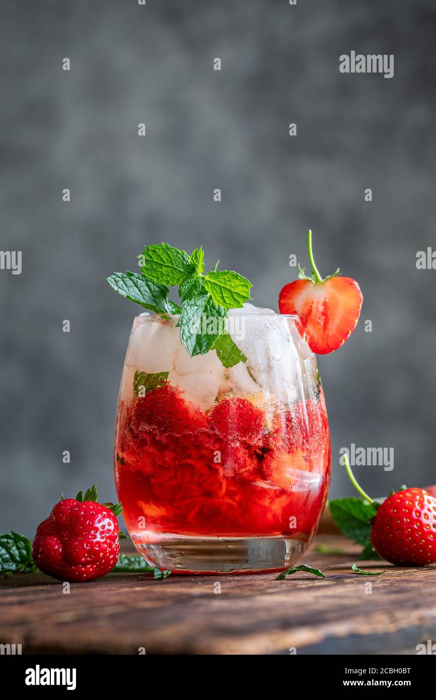 Un mojito fresco di fragola. Il cocktail o il mocktail si trova su un tavolo scuro in legno d'epoca. La bevanda è decorata con fragole e menta fresca. Foto Stock