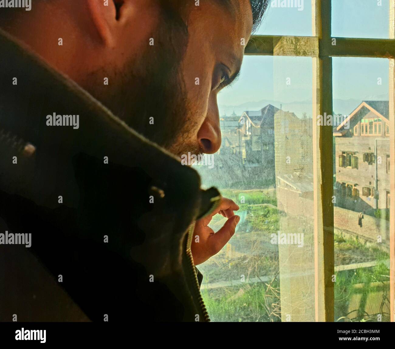 Una persona con maschera protettiva che guarda dalle finestre domestiche. La gente auto-isolando a casa, ha preso attraverso il loro specchio di finestre. Foto Stock