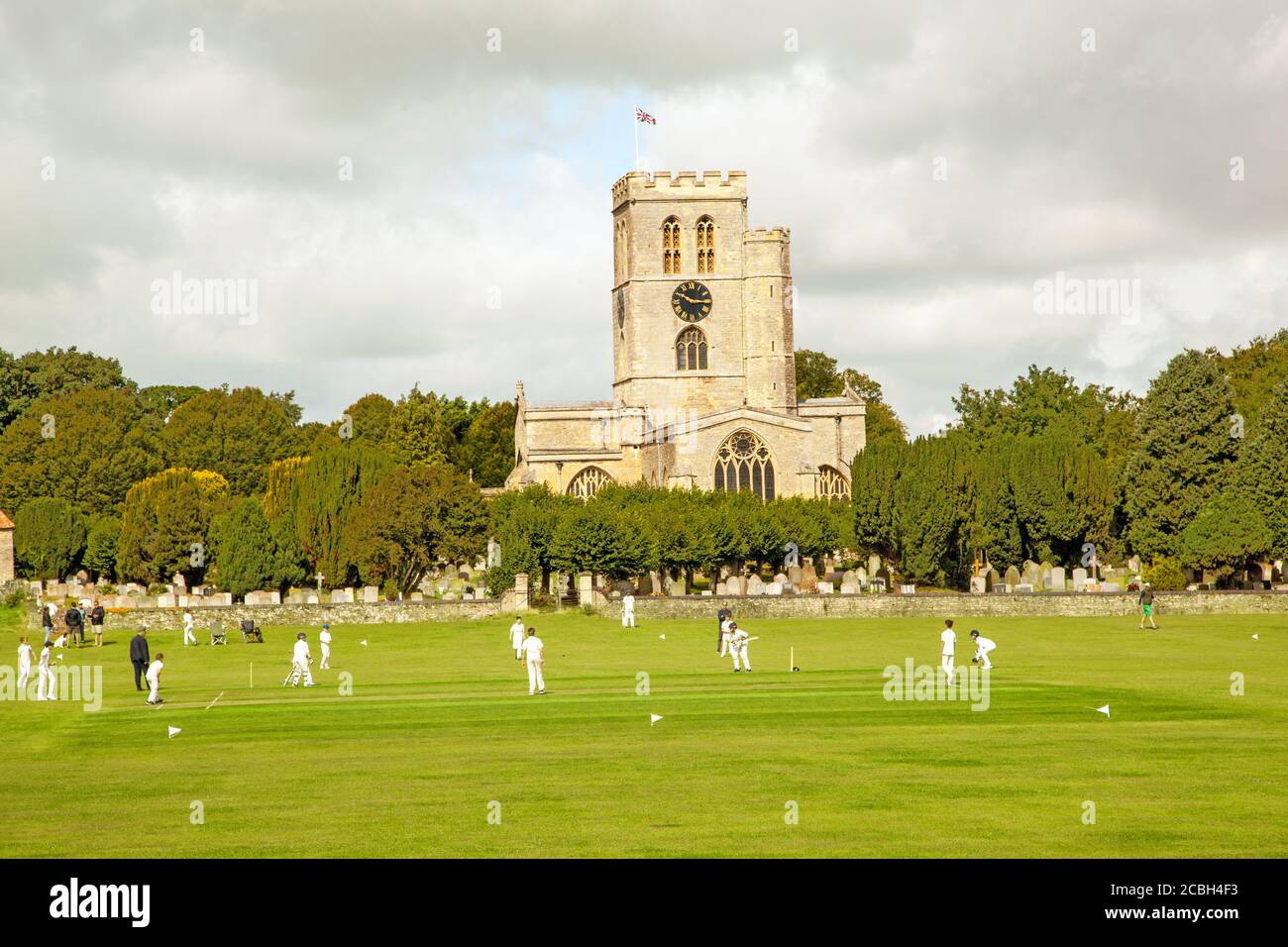 Junior partita di cricket giovani sul pittoresco prato della chiesa sede del club di cricket Thame Oxfordshire England con St Mary's. chiesa sullo sfondo Foto Stock