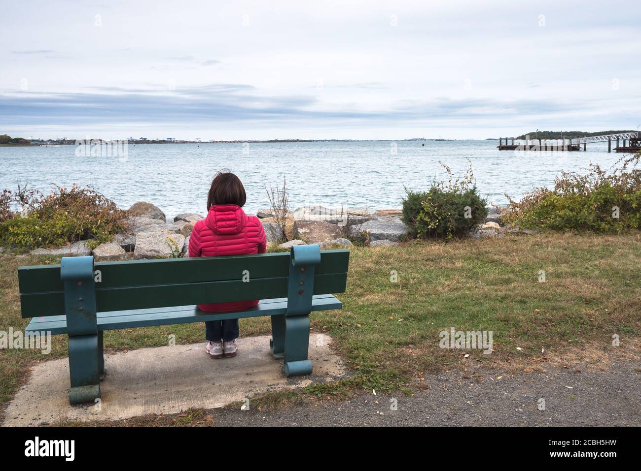 Donna solitaria seduta su una panchina di fronte ad una baia in un giorno nuvoloso d'autunno. Concetto di solitudine. Foto Stock