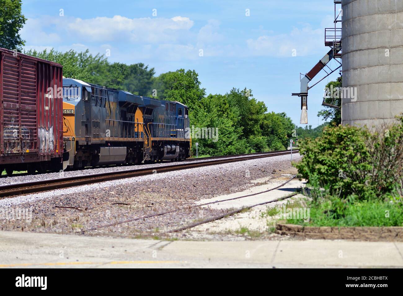 Watseka, Illinois, Stati Uniti. Un paio di locomotori conducono un treno merci manifesto CSX Transportation passando un elevatore di cereali a Wasteka, Illinois. Foto Stock