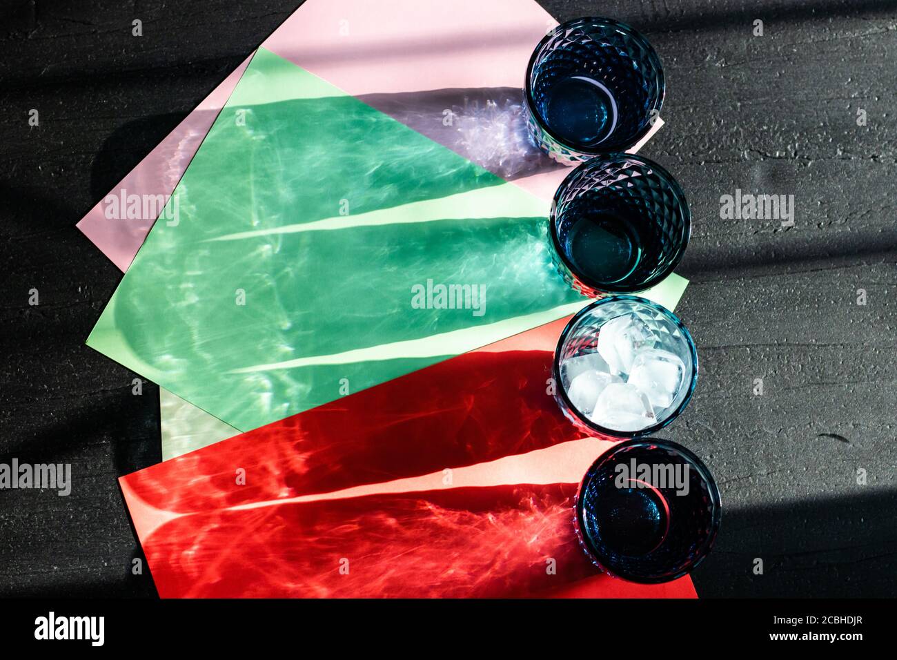 Ombra e luce giocano con sfumature di colore di occhiali blu su una carta colorata su uno sfondo nero. Foto Stock