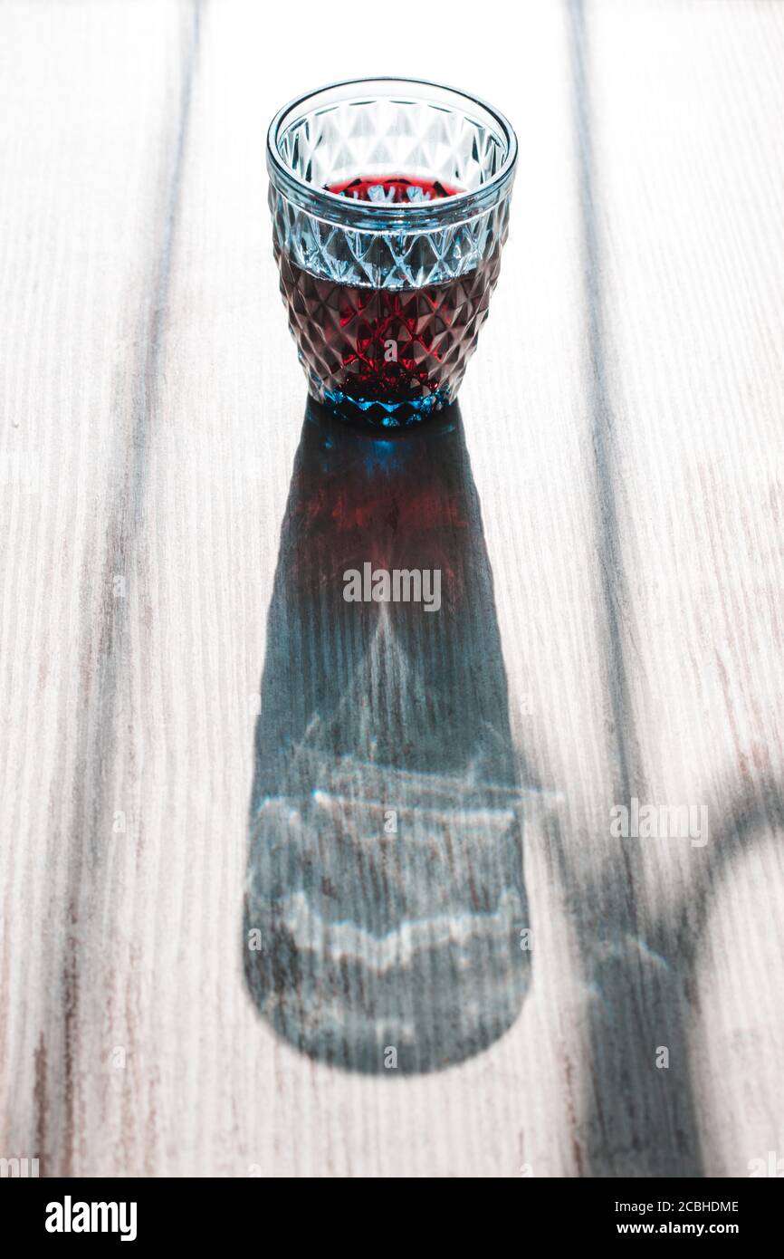 Illusione ottica visiva con luce e ombre gioco di duro la luce del sole splende attraverso un bicchiere di vino rosso cristallo blu Foto Stock