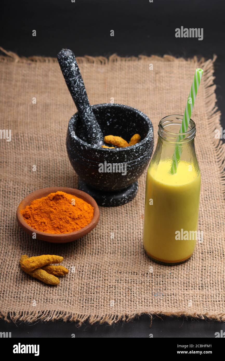 Bevanda curcuma, latte, tè, latte con cannella in tazza di vetro con curcuma fresco e secco. Foto Stock