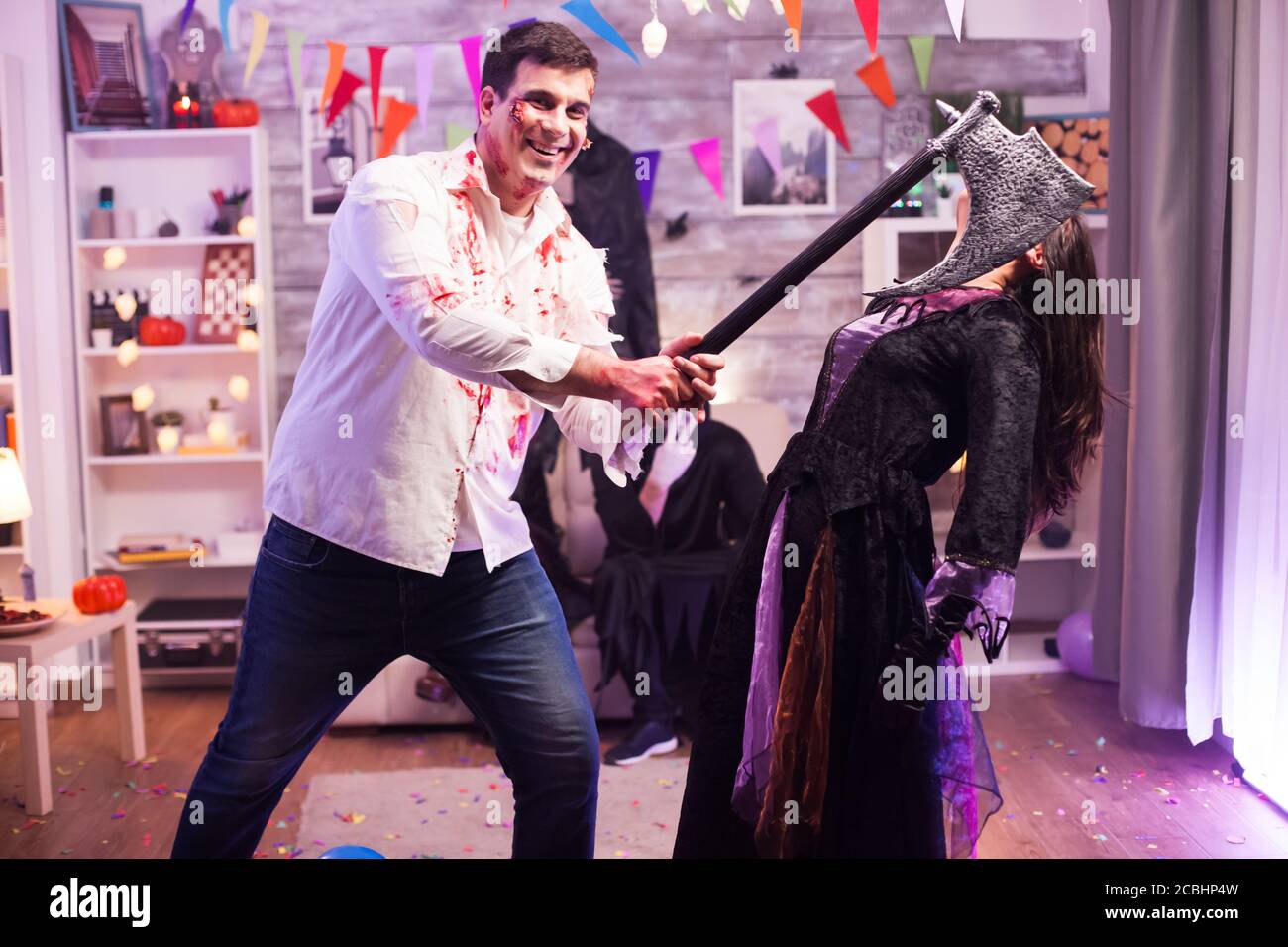 Uomo vestito come zombie con un'ascia che cerca di uccidere una strega malvagia durante la festa di Halloween. Foto Stock