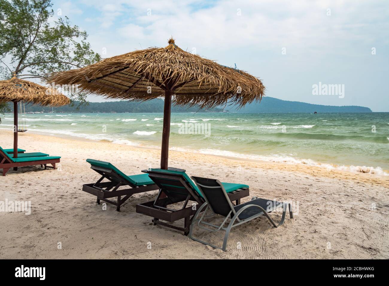 Spiaggia calma scena con lettini e ombrelloni di paglia sotto palme da cocco vicino al mare dei Caraibi. Paradiso tropicale con chaise lounges su sabbia bianca, no Foto Stock