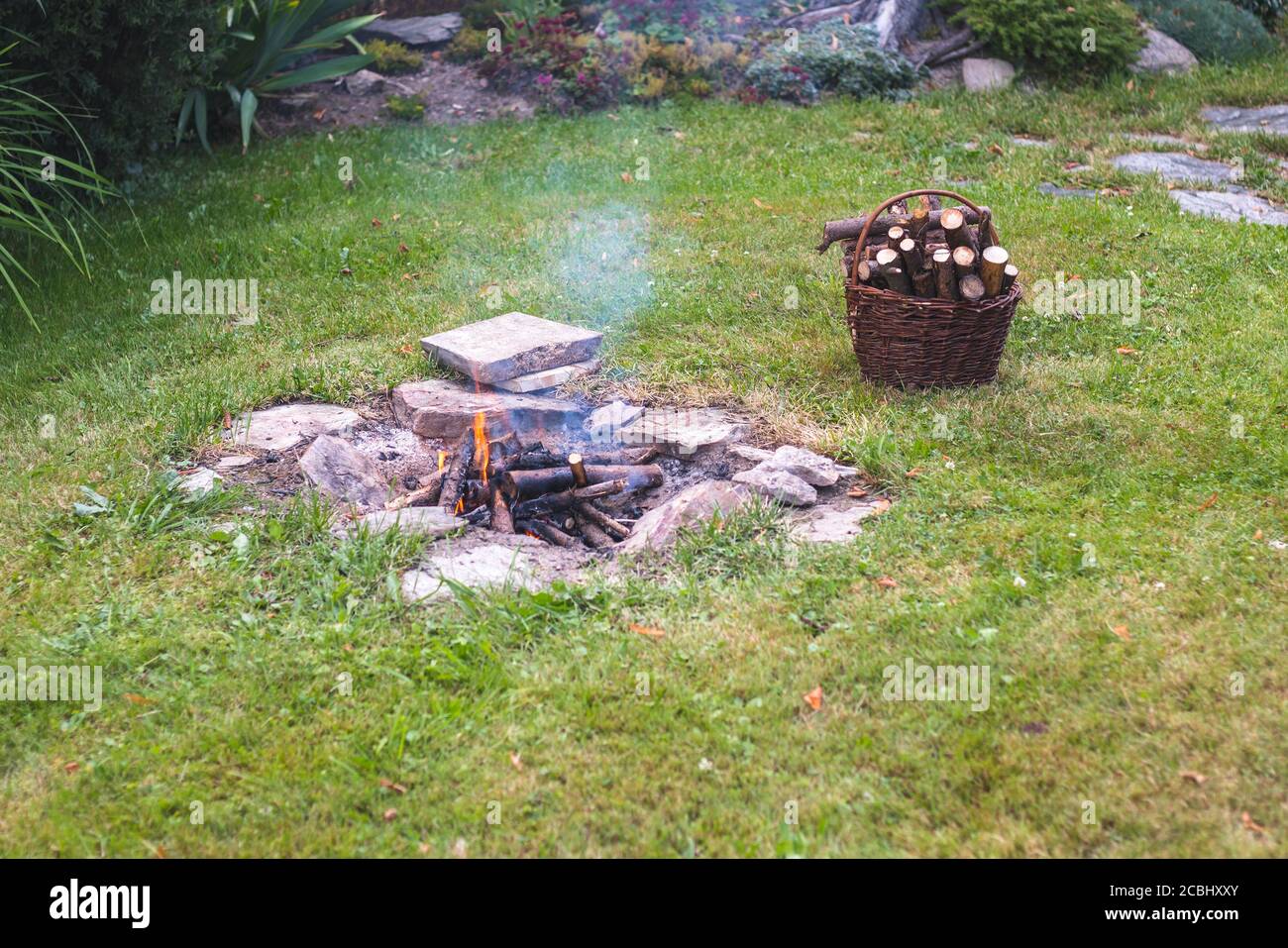 fuoco di campo nel giardino, accanto ad un cesto con legna da ardere Foto Stock