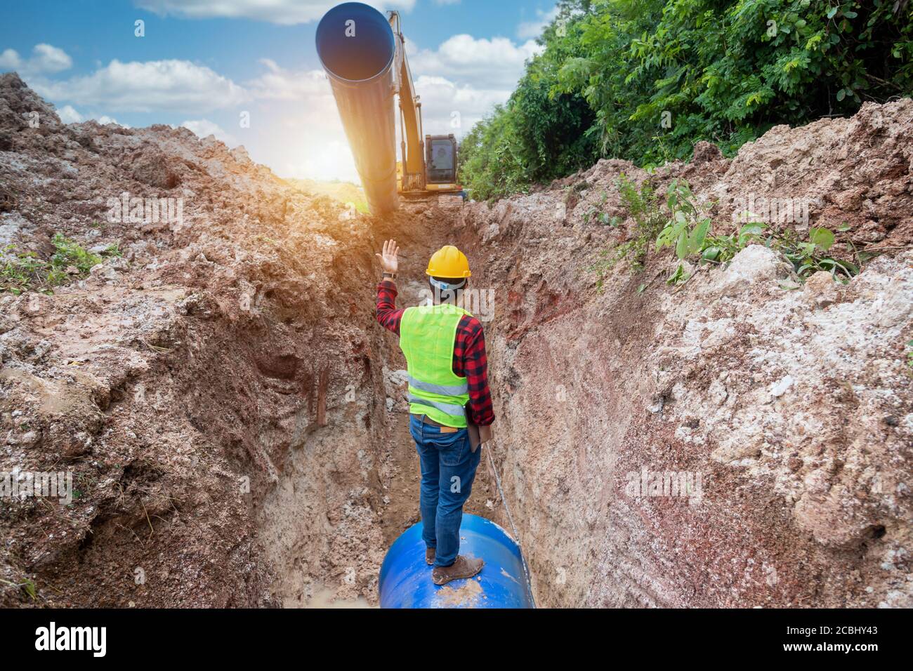 Il tecnico deve indossare l'uniforme di sicurezza esaminando il tubo di drenaggio dello scavo e l'impianto idraulico di grandi dimensioni interrato nel cantiere. Foto Stock