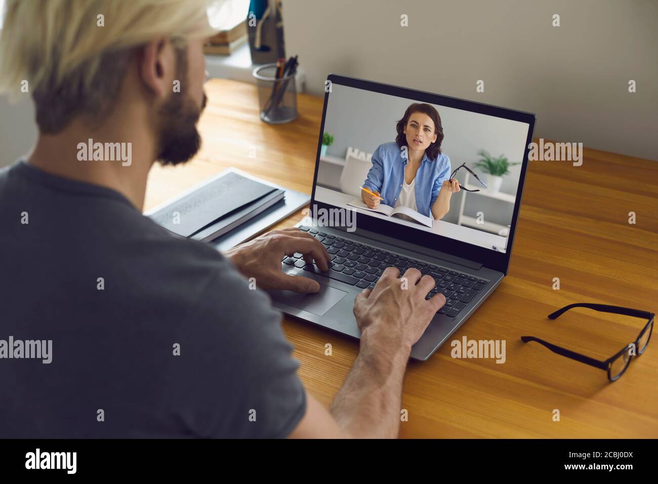 Formazione e lavoro online. Giovane seduto a casa alla sua scrivania e utilizzando la videochiamata sul laptop per lo studio e il lavoro. Foto Stock
