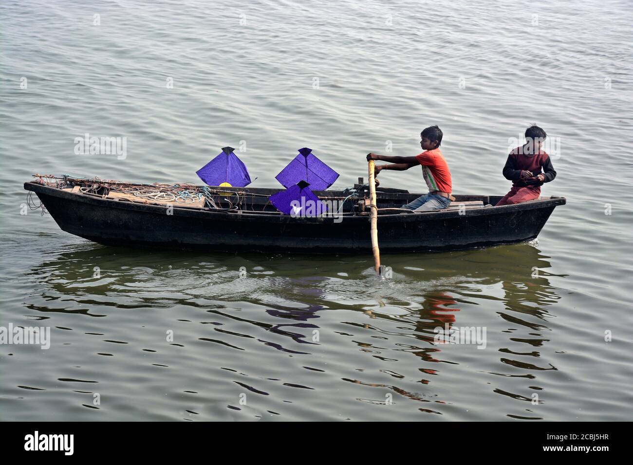 A Varanasi, due ragazzi stanno raccogliendo aquiloni dal fiume Gange e lo lasciano in barca. Molti aquiloni sono volati a Varanasi in inverno. Foto Stock