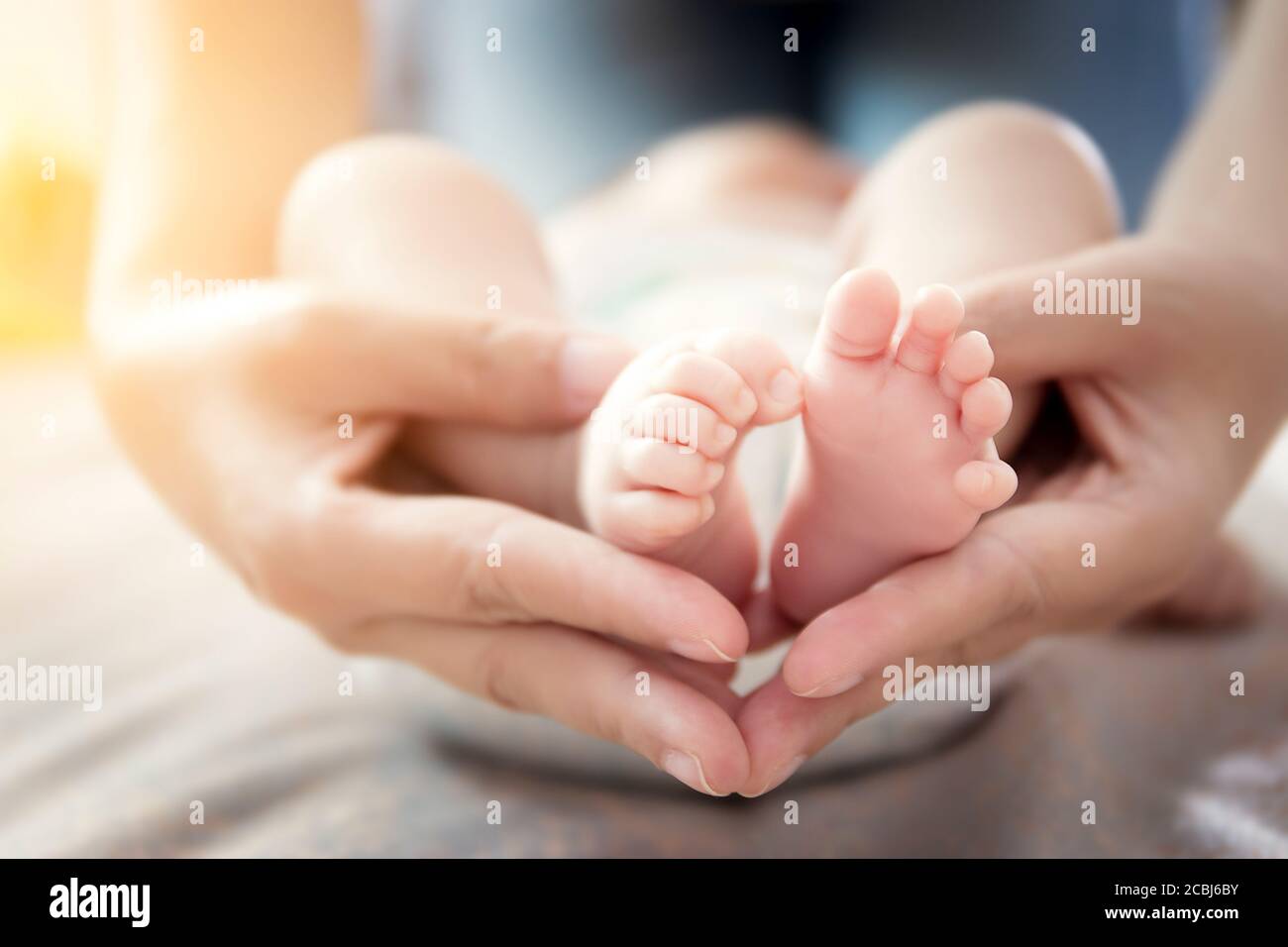 Buon rapporto nel concetto di famiglia : i piedi del bambino del neonato nelle mani della madre. Il genitore tiene i piedi piccoli del bambino neonato nelle mani con cura delicata Foto Stock