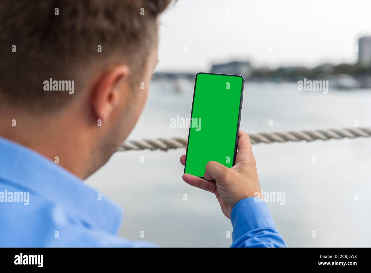 Uomo che tiene uno smartphone con schermo verde in mano accanto al fiume. Copiare spazio, aggiungere testo, foto o logo Foto Stock