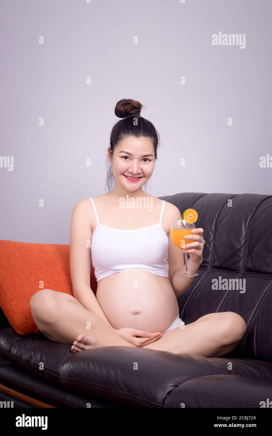 Donna incinta mangiare cibo con ingrediente per un concetto sano: Giovane donna incinta asiatica tenere fresco succo d'arancia in vetro con sorriso amichevole faccia Foto Stock