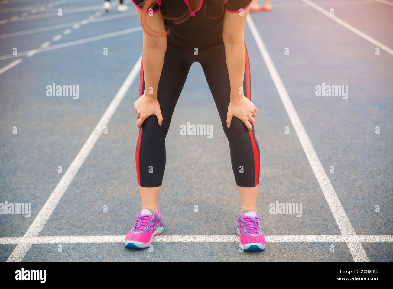 Atleta di runner femminile lesioni al ginocchio e dolore. Donna che soffre di ginocchio doloroso mentre corre sulla pista blu gommata. Foto Stock