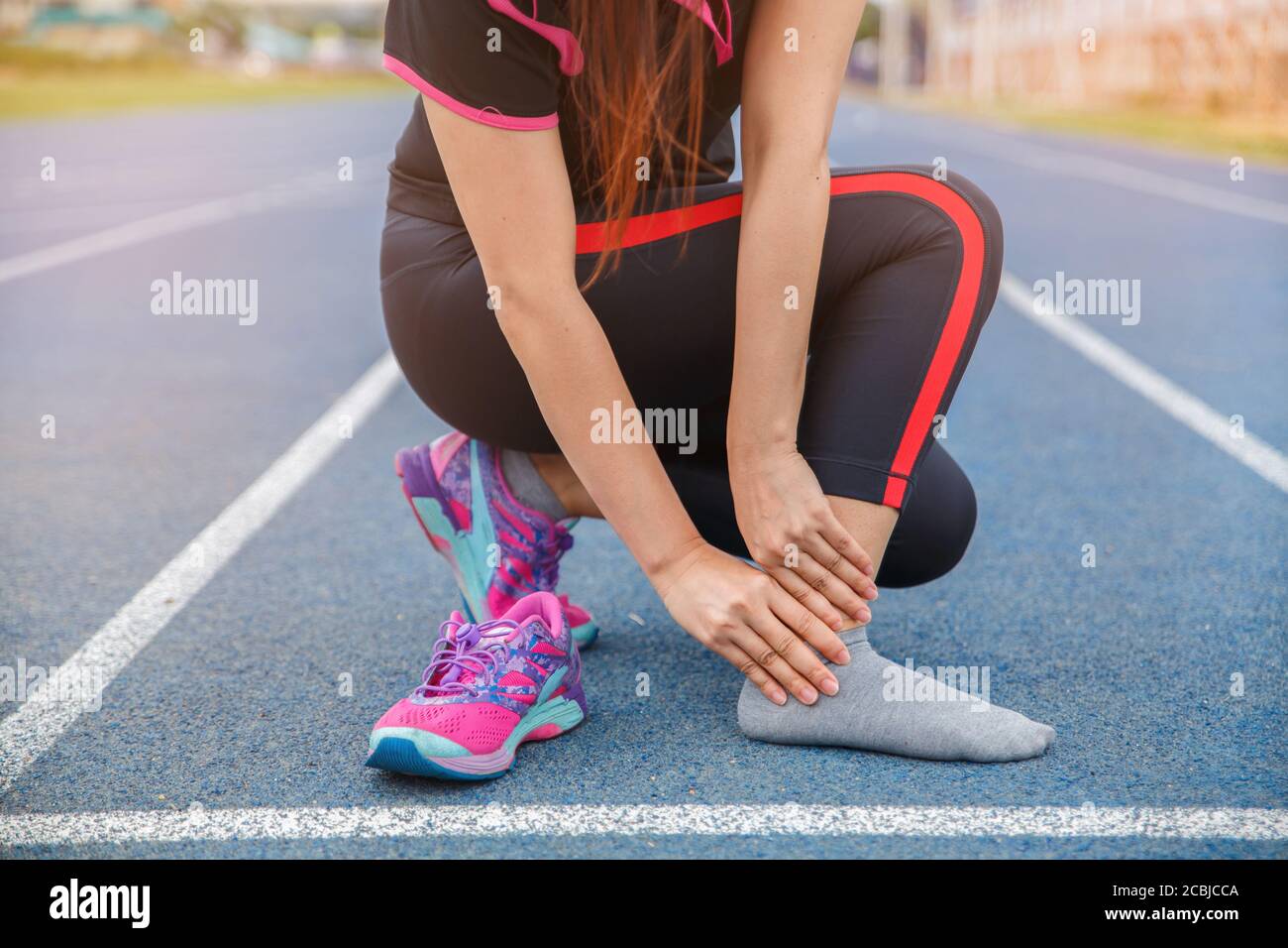 Donna atleta di runner ferita e dolore alla caviglia. Donna che soffre di caviglia dolorosa mentre corre sulla pista blu gommata. Foto Stock