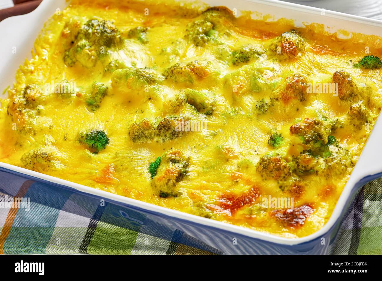 Primo piano di Cheesy Cheddar Broccoli Casserole in una teglia su un tavolo di legno, vista orizzontale dall'alto, macro Foto Stock