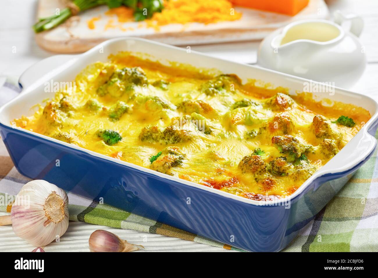 Primo piano di Cheesy Cheddar Broccoli Casserole in una teglia da forno su un tavolo di legno con ingredienti sullo sfondo, vista orizzontale dall'alto Foto Stock