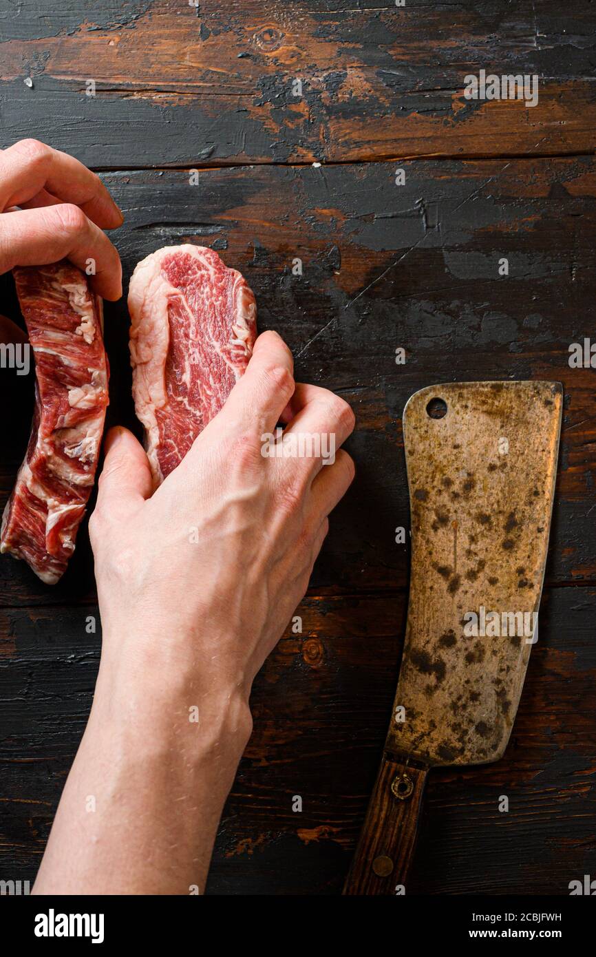 Fresco Chuck eye roll Black angus marmorizzato bistecca di manzo su tavola vintage di legno scuro manzo organico. Con le mani macellaio e sfaldatura di carne al lavoro Foto Stock