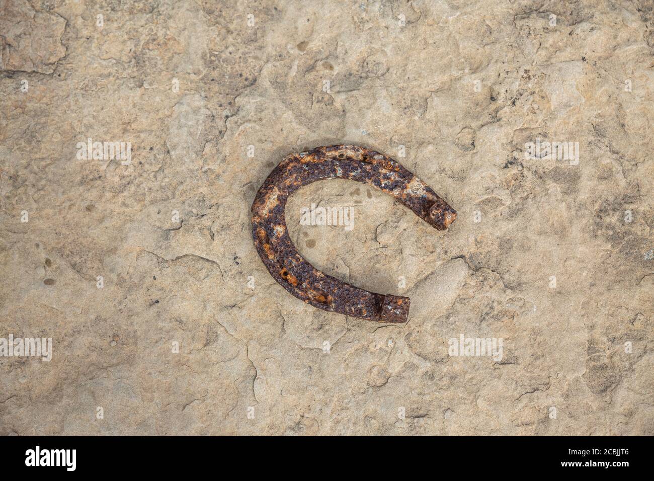 Un vecchio ferro di cavallo arrugginito proppato su una grande pietra. Simbolo di felicità e fortuna. Foto Stock
