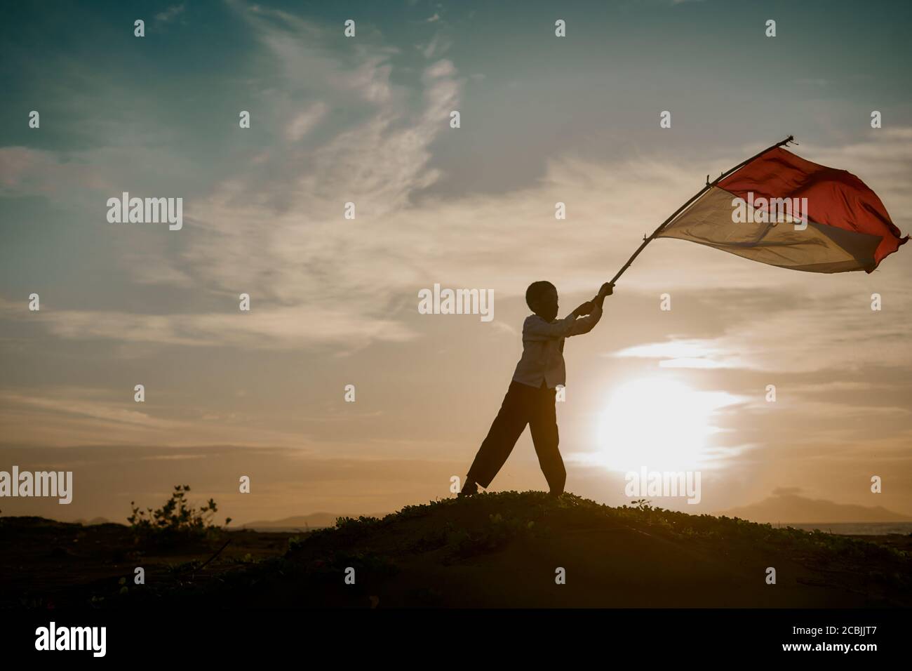 Little Boy sventolando bandiera indonesiana rossa e bianca al tramonto natura Foto Stock