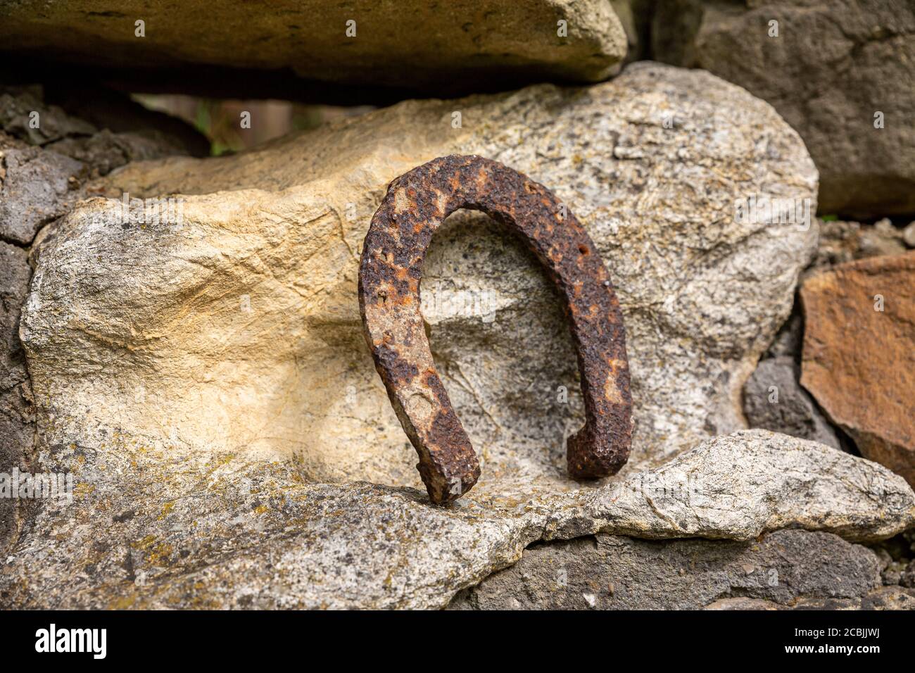 Un vecchio ferro di cavallo arrugginito proppato su una grande pietra. Simbolo di felicità e fortuna. Foto Stock