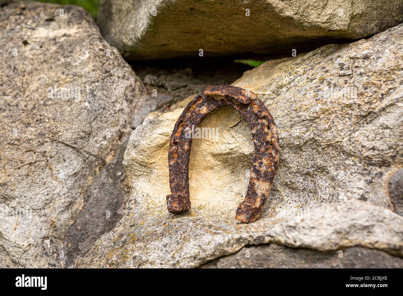 Un vecchio ferro di cavallo arrugginito proppato su una grande pietra. Simbolo di felicità e fortuna. Foto Stock