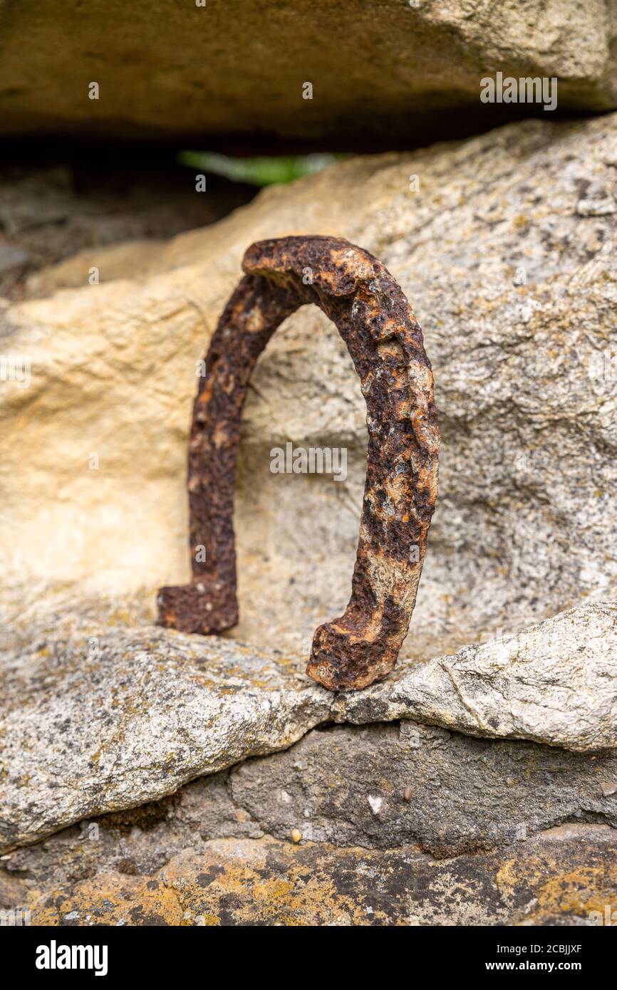Un vecchio ferro di cavallo arrugginito proppato su una grande pietra. Simbolo di felicità e fortuna. Foto Stock