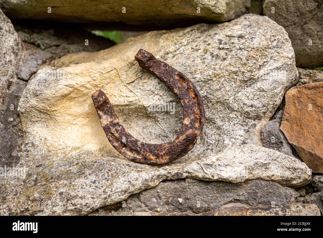 Un vecchio ferro di cavallo arrugginito proppato su una grande pietra. Simbolo di felicità e fortuna. Foto Stock