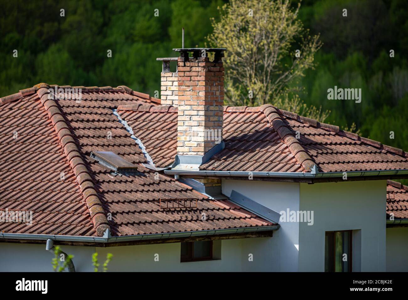 Un frammento di tetto in tegole con camino e finestre in una nuova casa nei boschi del villaggio bulgaro. Foto Stock