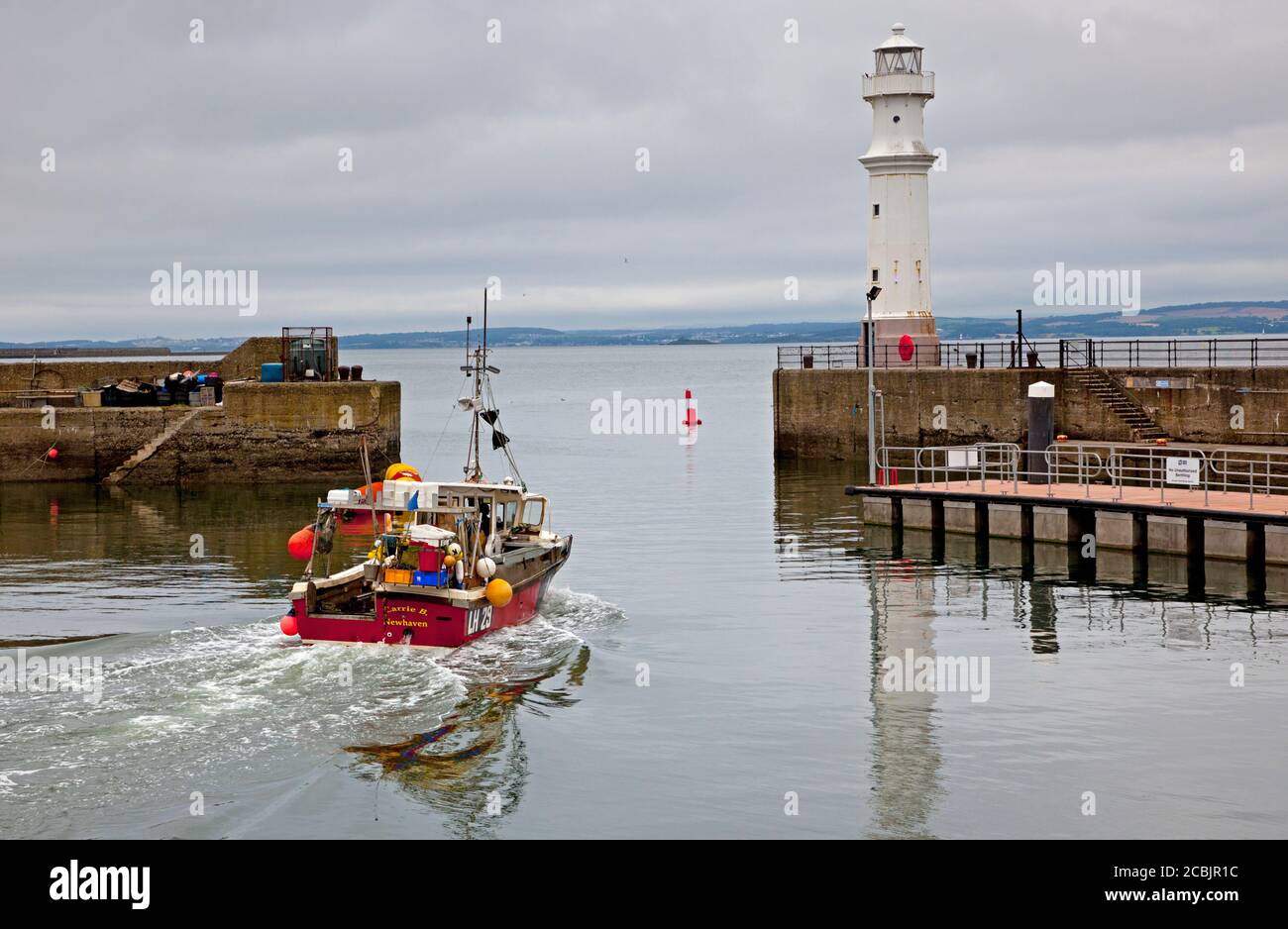 Newhaven Harbour, Edimburgo, Scozia, Regno Unito. 14 agosto 2020. Temperatura 17 gradi e tempo denso nuvoloso come la barca da pesca Carrie B si propone per il lavoro nel Firth of Forth con il faro sulla destra del piccolo porto. Solo questa mattina le autorità sanitarie di Orkney hanno riferito che si stanno occupando di un gruppo di cinque casi confermati di Covid-19 collegati a una barca da pesca, illustrando potenziali pericoli per l'equipaggio di imbarcazioni da pesca. Foto Stock