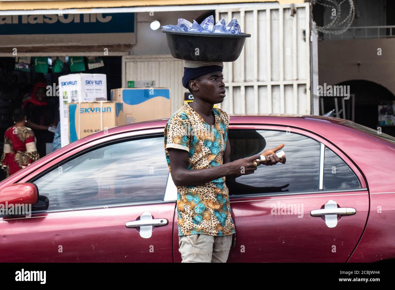 Ragazzo che vende acqua pura. Un ragazzo africano che vende acqua pura sulla strada accanto a un'auto rossa, Foto Stock