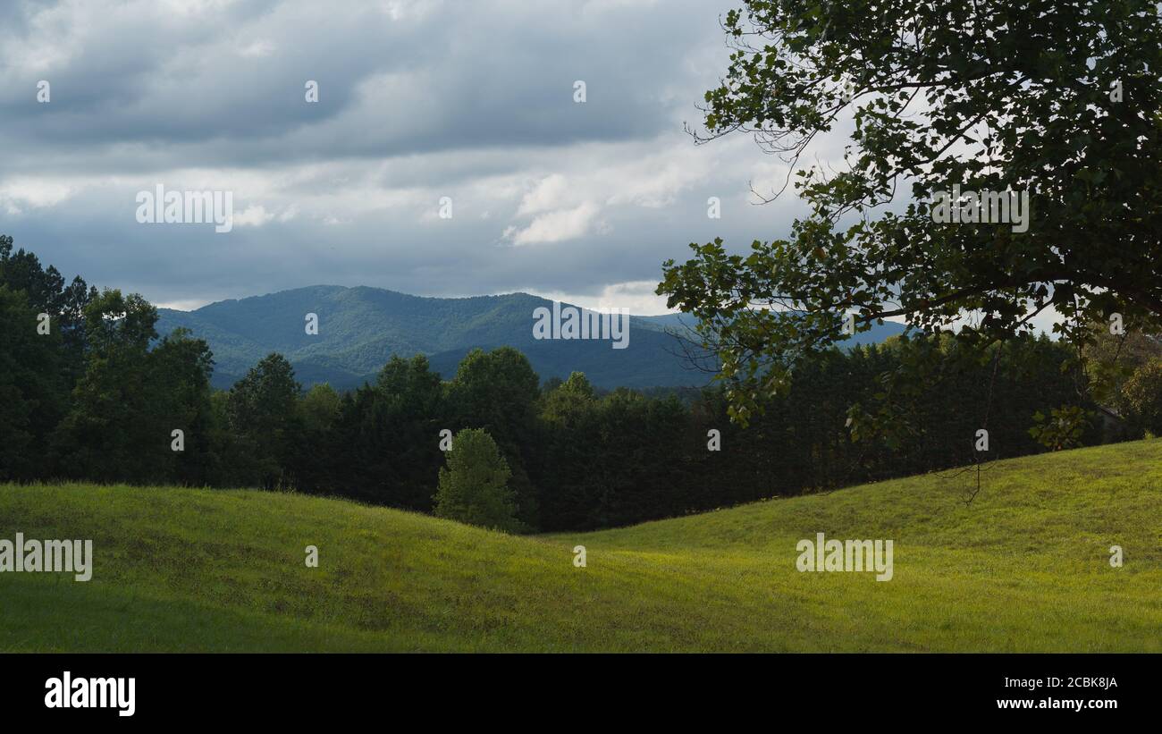 Nuvole colorate sopra le belle Blue Ridge Mountains con un prato verde in primo piano Foto Stock