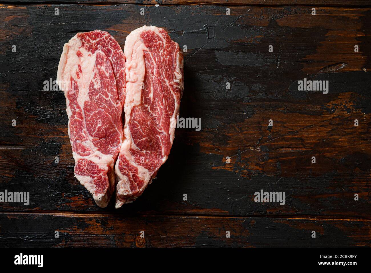 Heartshape Raw Chuck bistecca di manzo su tavola di legno scuro vintage manzo organico. Vista dall'alto nera. Spazio per il testo Foto Stock