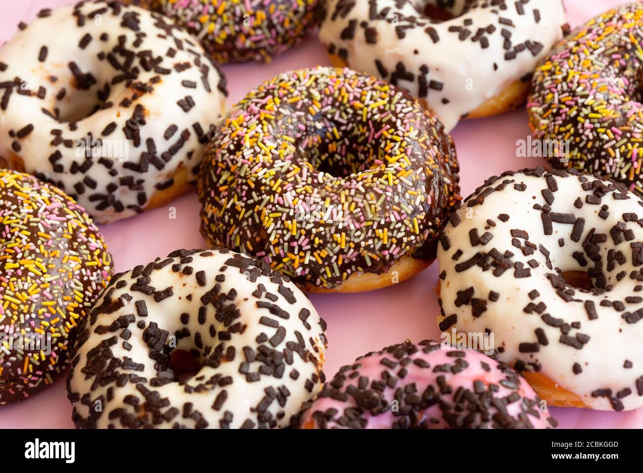 Primo piano vista di deliziose ciambelle colorate con spruzzi e fiocchi di cioccolato . Ciambelle assortite con glassa al cioccolato, glassa bianca e rosa e spolverate. Messa a fuoco selettiva. Foto Stock