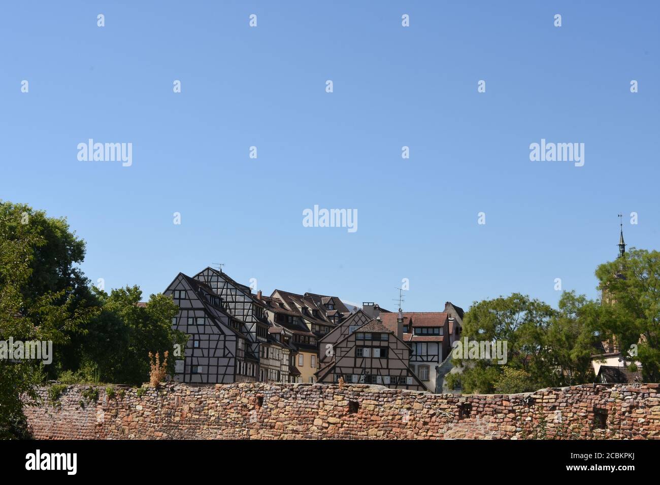 Edifici medievali e del primo Rinascimento a graticcio dietro le mura di mattoni rossi sotto il cielo blu a Colmar, una città nella regione del Grand Est della Francia. Foto Stock