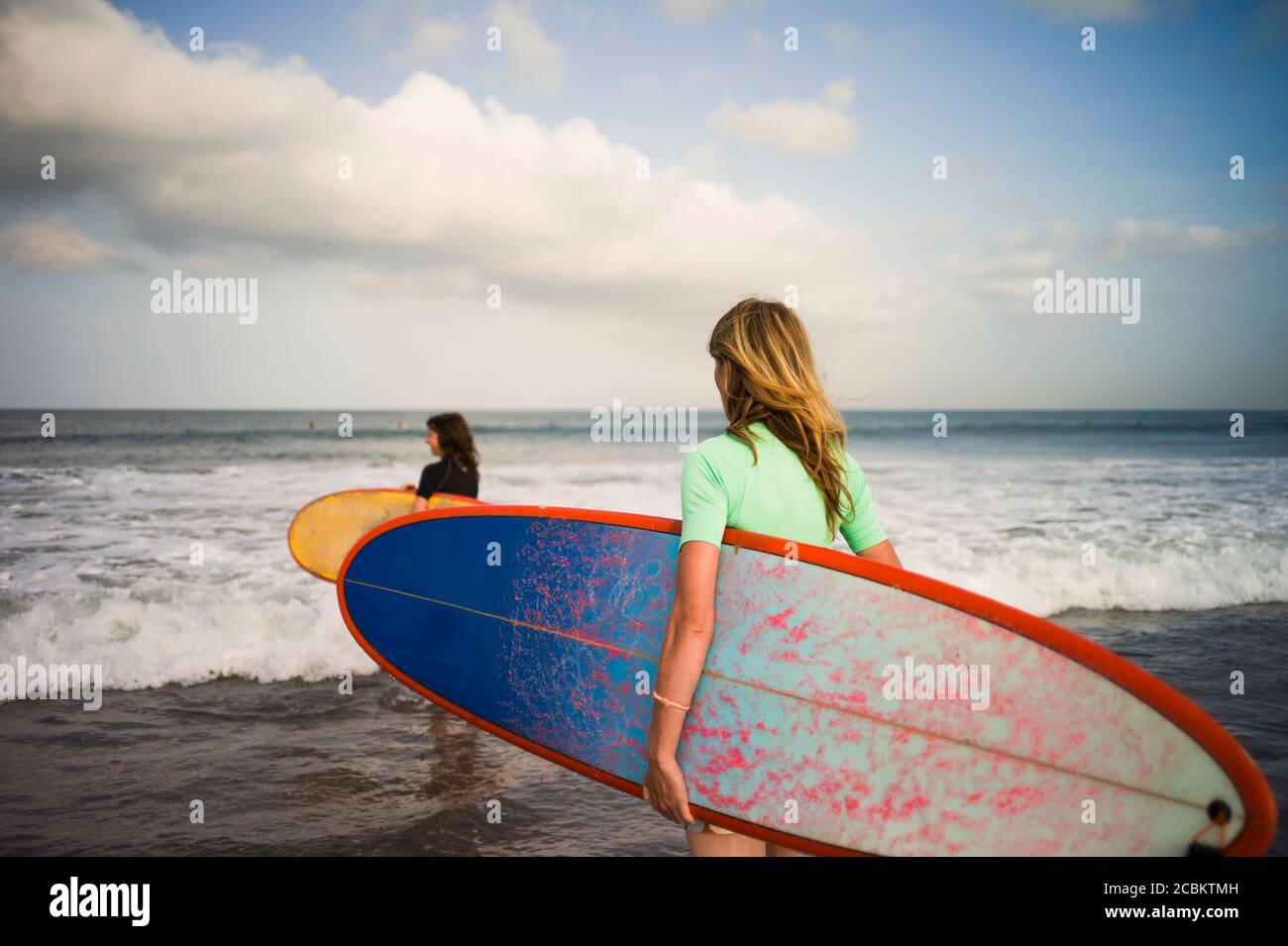 Due donne che camminano verso il mare, portando tavole da surf, Seminyak, Bali, Indonesia Foto Stock