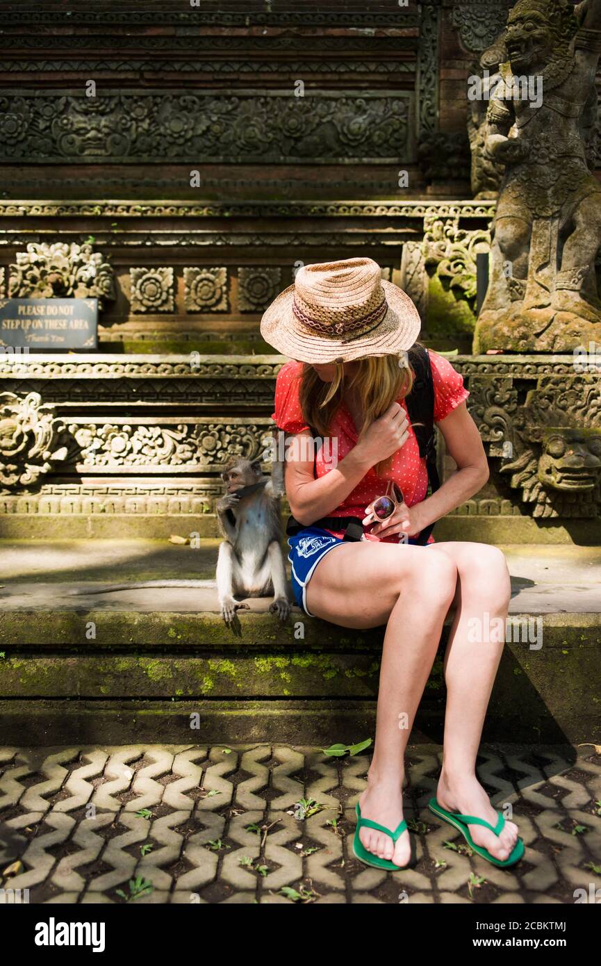 Donna mid adulta seduta su gradini, scimmia seduta accanto a lei, Ubud, Bali, Indonesia Foto Stock
