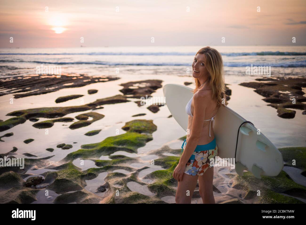 Donna che tiene la tavola da surf, che cammina verso il mare, Balangan, Bali, Indonesia Foto Stock