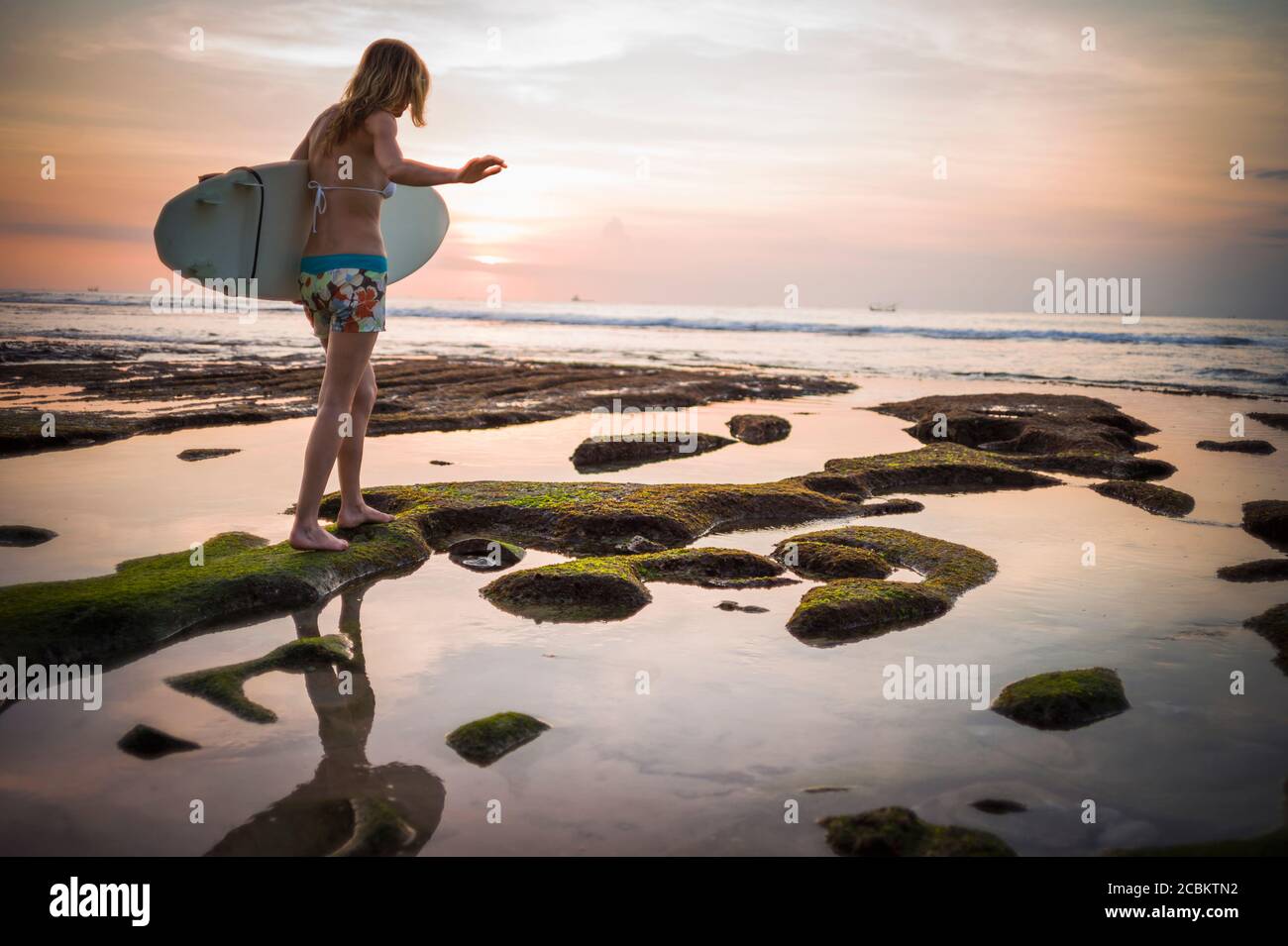 Donna che tiene la tavola da surf, che cammina verso il mare, Balangan, Bali, Indonesia Foto Stock