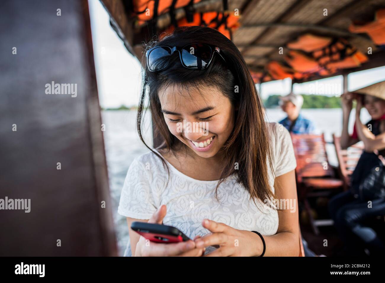 Donna che guarda la foto nel telefono cellulare su nave da crociera, Delta Mekong, Vietnam Foto Stock