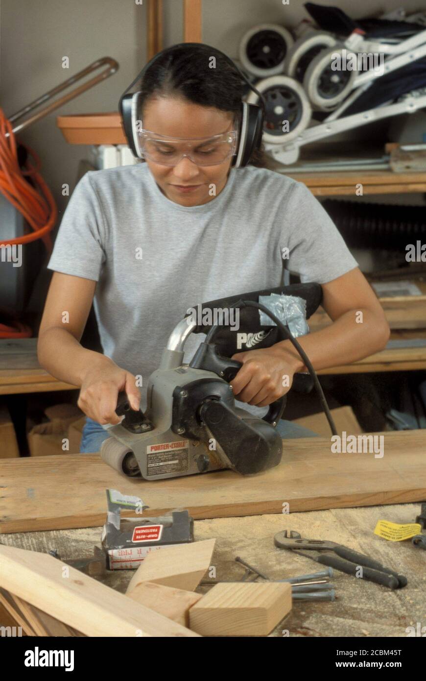 Austin, Texas USA, 1996: La donna afroamericana utilizza una levigatrice a nastro elettrica mentre indossa occhiali protettivi e copriauricolari. Modello rilasciato ©Bob Daemmrich Foto Stock