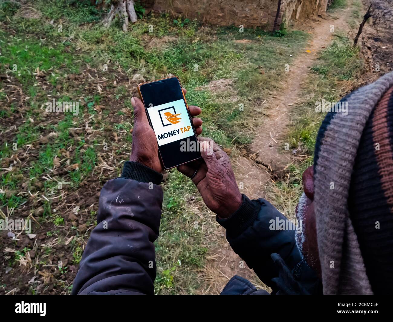 DISTRETTO KATNI, INDIA - 20 DICEMBRE 2019: Denaro Tap logo prestito istantaneo presentato su smart phone schermo digitale da parte della gente villaggio indiano mano che tiene m Foto Stock