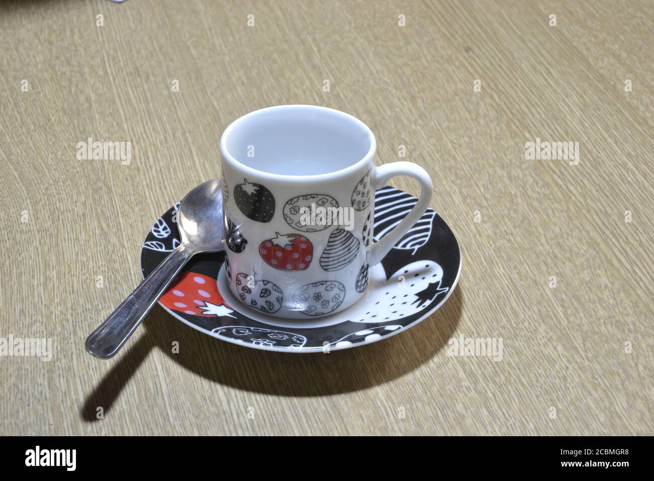 Tazza di caffè multicolore con piattino come base con disegni colorati e cucchiaio su sfondo di legno. Foto Stock