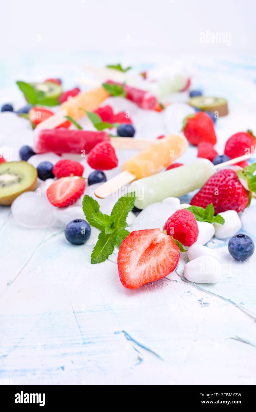 Papicle di frutta intera sane con fragole di Berries Kiwi su sfondo chiaro con un decor di ghiaccio, menta. Gustoso gelato alla frutta nella tazza. Spazio di copia. Foto Stock