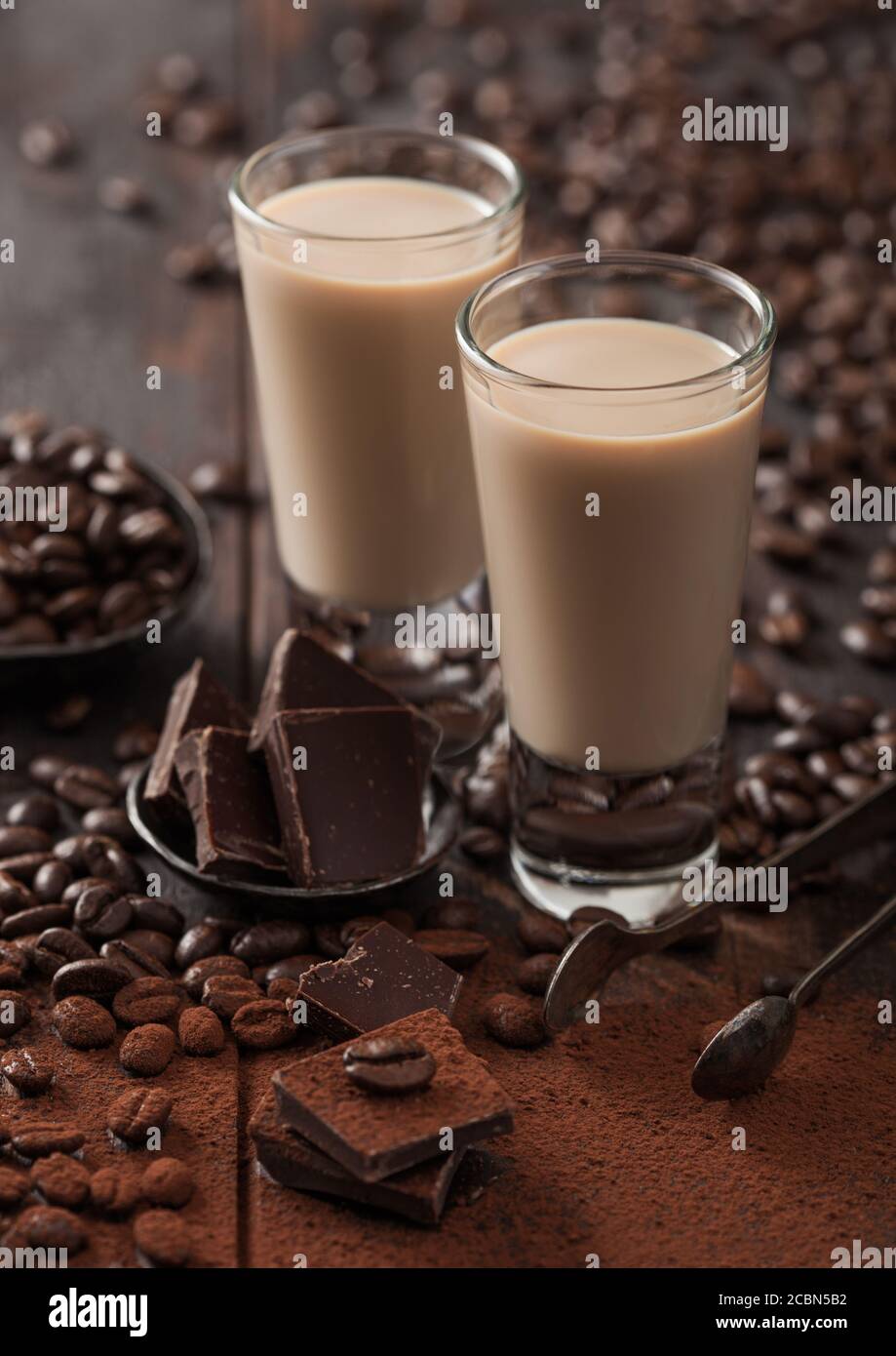 Bicchieri da shot di liquore irlandese baileys con chicchi di caffè e polvere con cioccolato fondente su sfondo di legno scuro. Macro Foto Stock