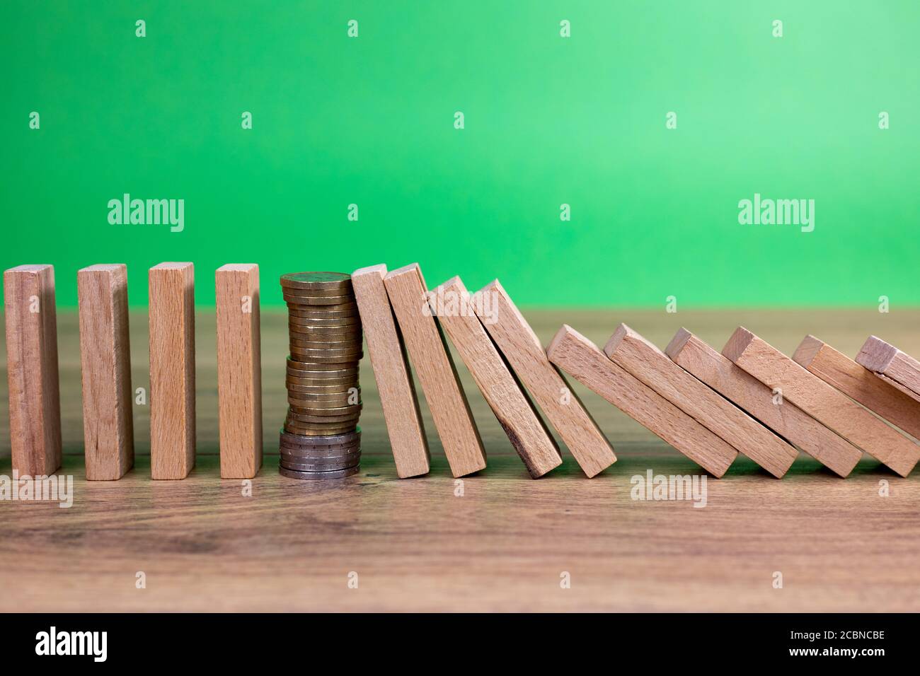 concetto di effetto domino con piastrelle di legno bloccate da moneta con sfondo verde Foto Stock